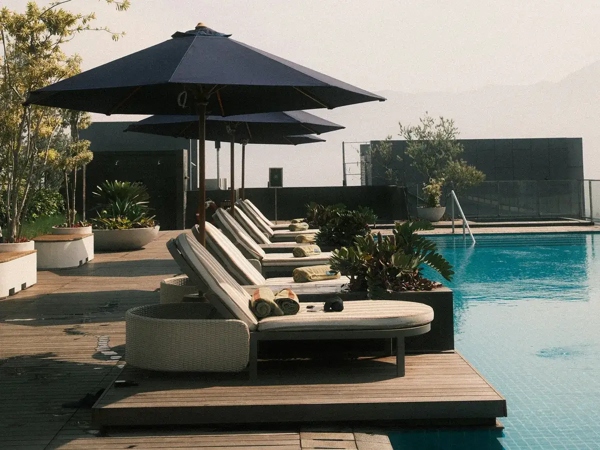 Piscină cu apa la cota terasei, șezlonguri și umbrele pe deckul din lemn